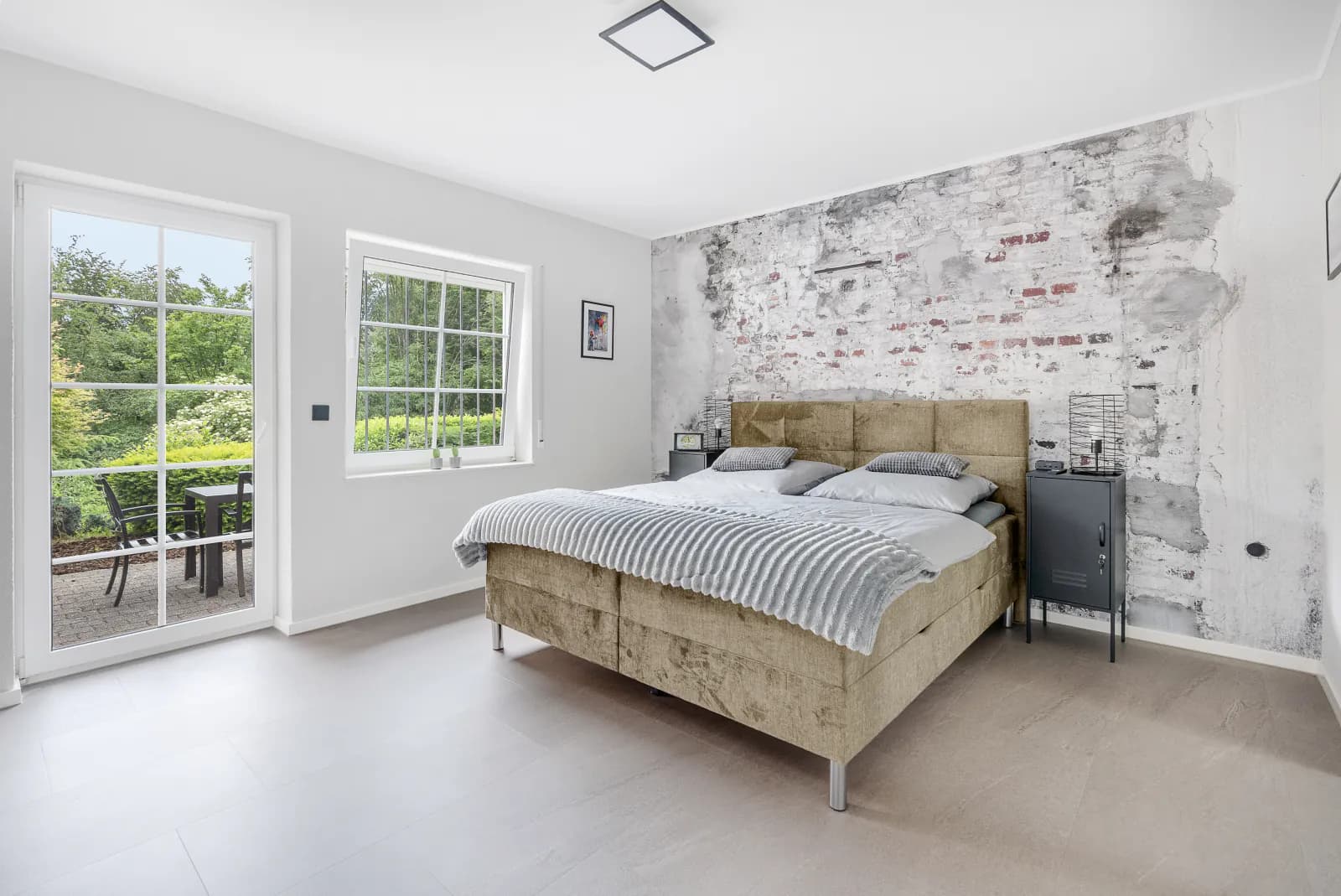 Helles Schlafzimmer mit Boxspringbett, Backstein-Akzentwand und Gartenblick durch die Terrassentür