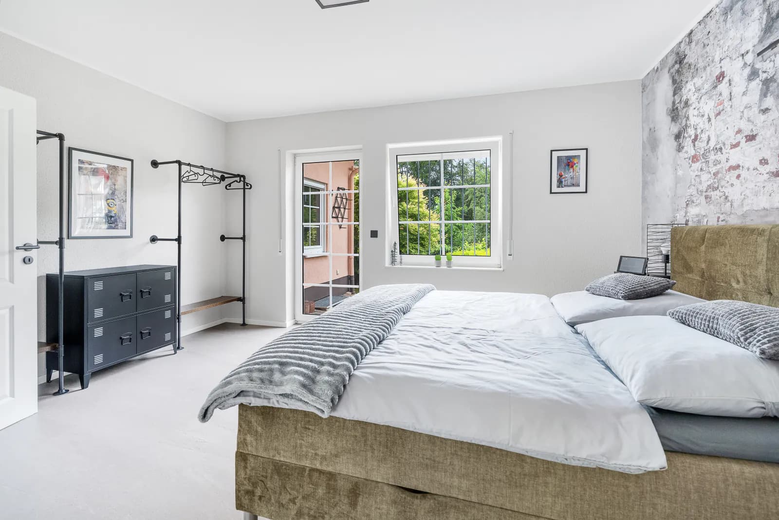 Schlafzimmer mit Boxspringbett, Backsteinwand und offener Kleiderstange sowie Tür zur Terrasse